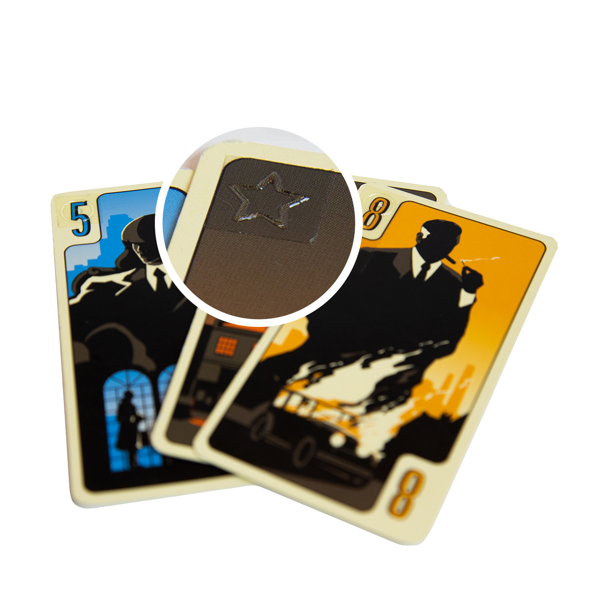 Deux cartes à jouer District noir montrent des silhouettes en costume, l'une bleue avec un 5 et l'autre jaune avec un 8. Un agrandissement révèle un détail étoilé en relief sur la surface de la carte, ce qui renforce l'esthétique noire du jeu.