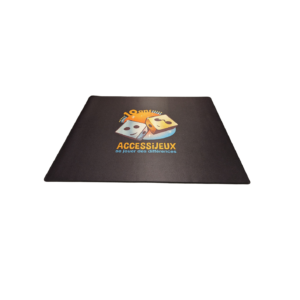 Un tapis rectangulaire noir portant le logo AccessiJeux, avec deux dés et un texte en français, est centré sur un fond blanc uni.
